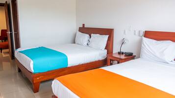 Habitación de hotel con dos camas, cada una con cabecero de madera, ropa de cama blanca y una manta azul y naranja. Hay una mesita de noche con una lámpara y un enchufe entre las camas.