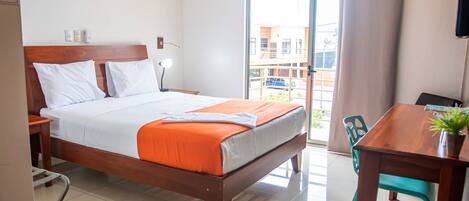 Habitación de hotel con una cama de madera, un escritorio con una silla, una planta en maceta y vistas al balcón exterior.