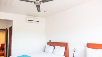 Ein Hotelzimmer mit einem Bett, einem Deckenventilator, einer Klimaanlage, einem Nachttisch mit Lampe und einem roten Sessel.