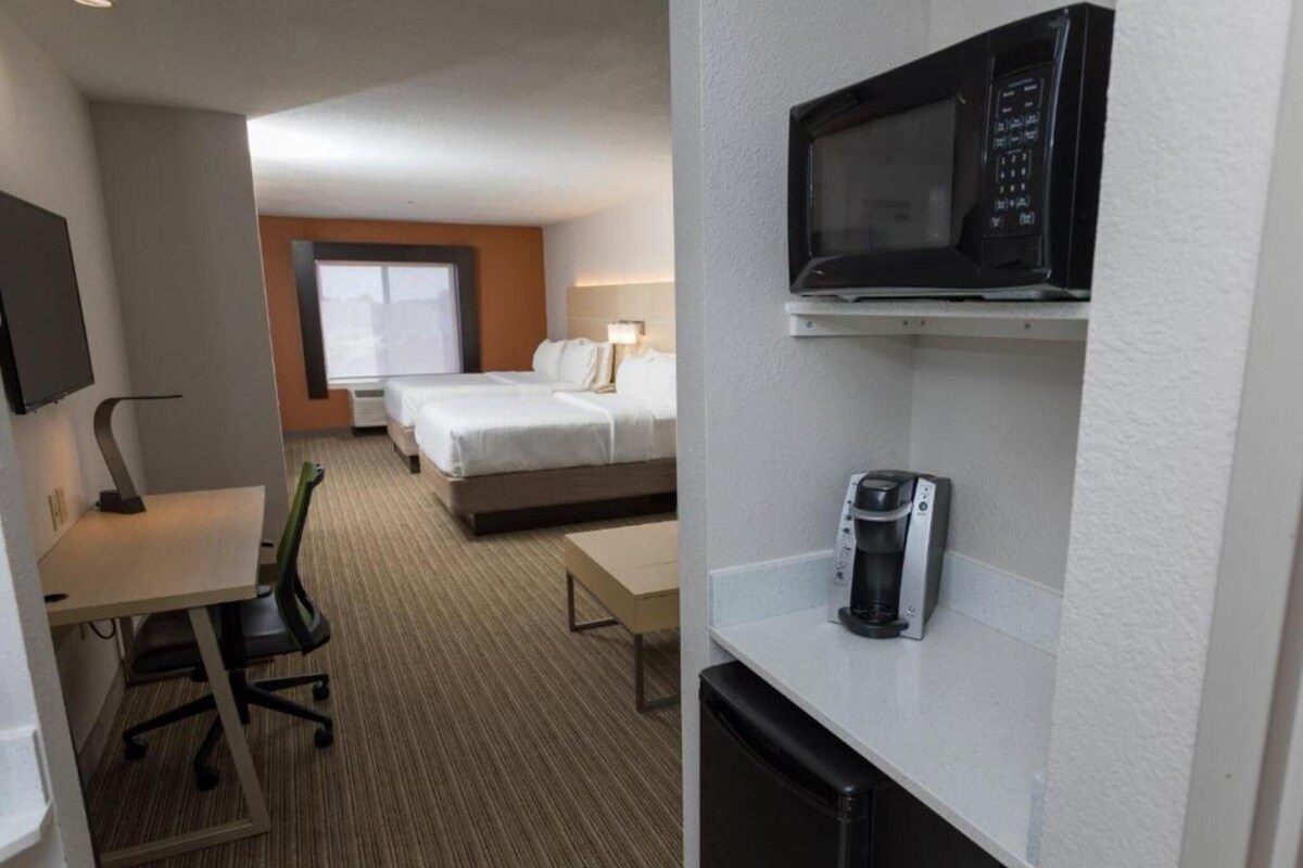 A hotel room with a desk, chair, two beds, a microwave, and a coffee maker.