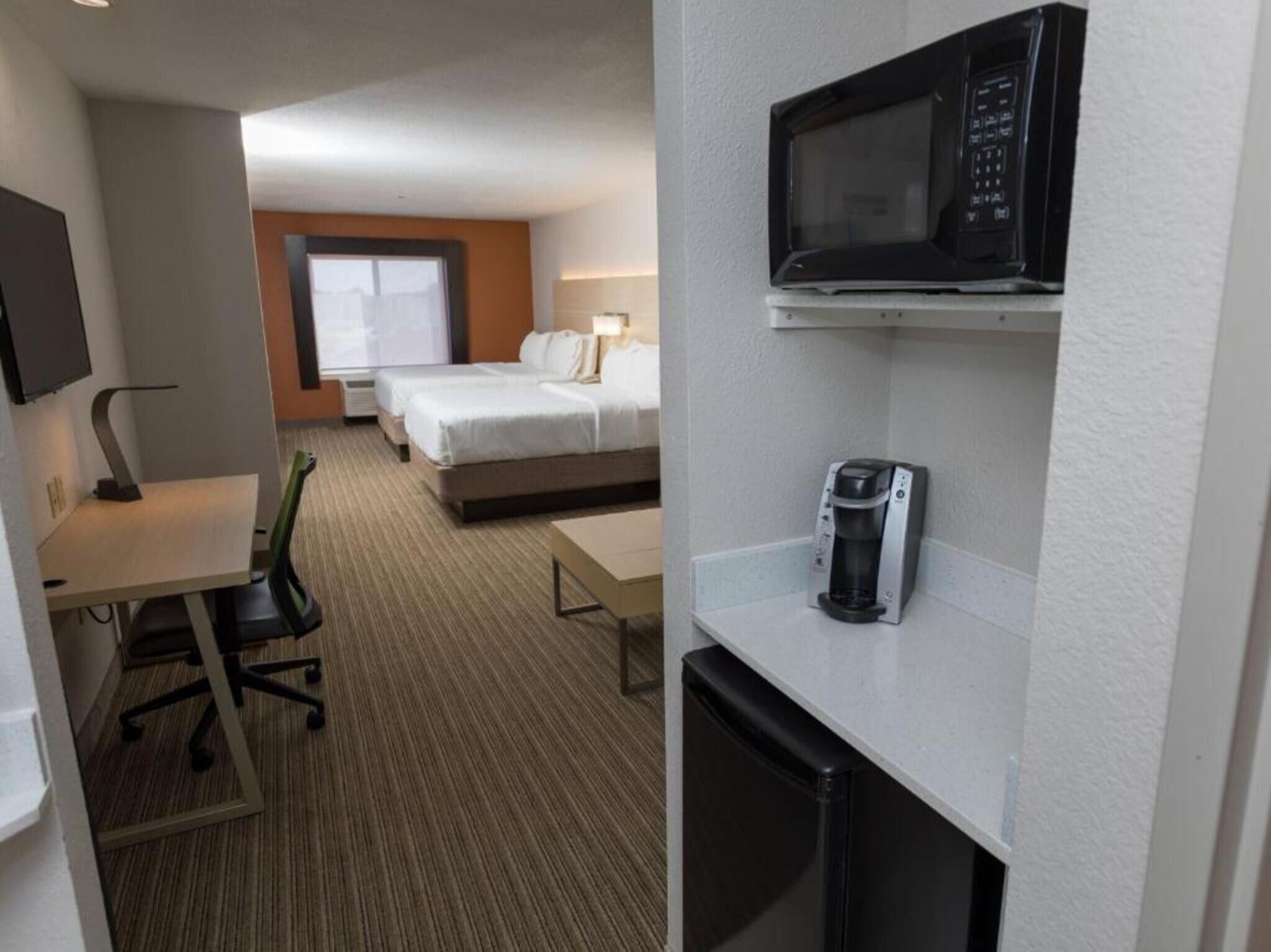 Habitación de hotel con escritorio, silla, dos camas, microondas y cafetera.