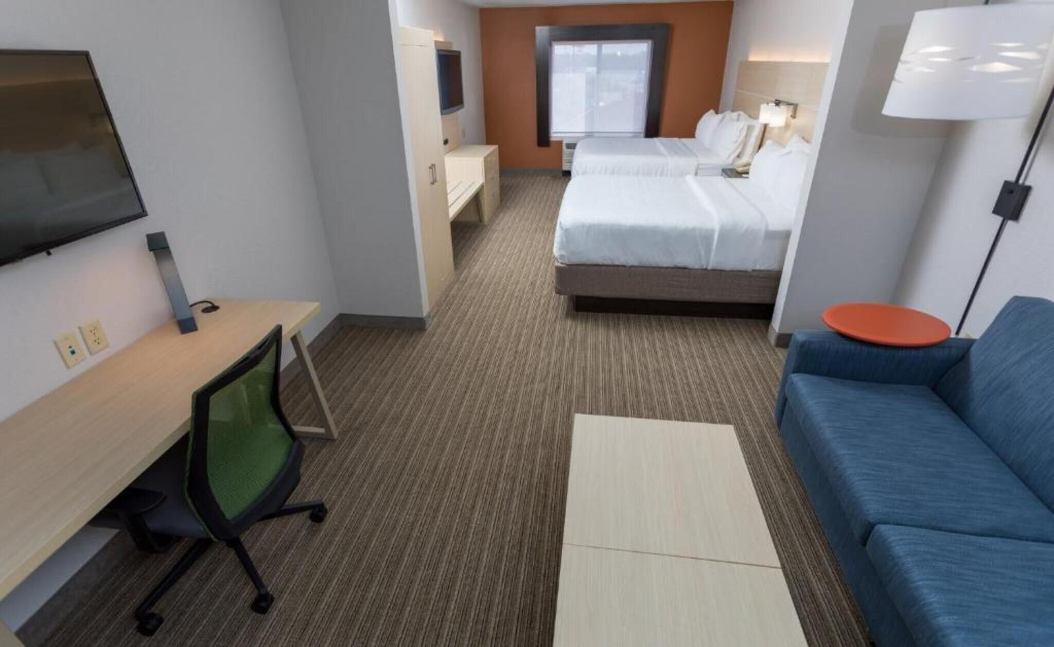Una habitación de hotel con una cama, un escritorio con silla, un sofá, un televisor y una ventana.