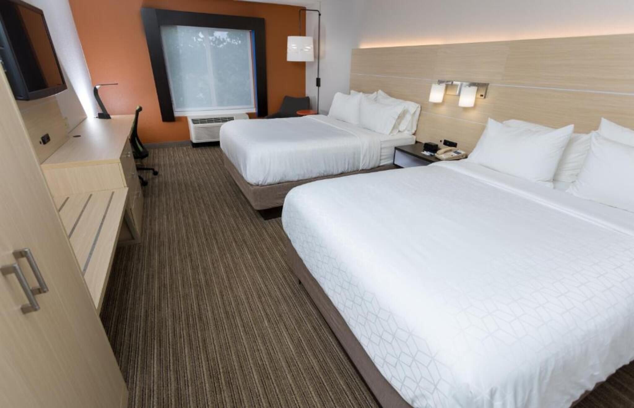 Habitación de hotel con dos camas, un escritorio, una silla, un ventanal y una lámpara fijada a la pared.