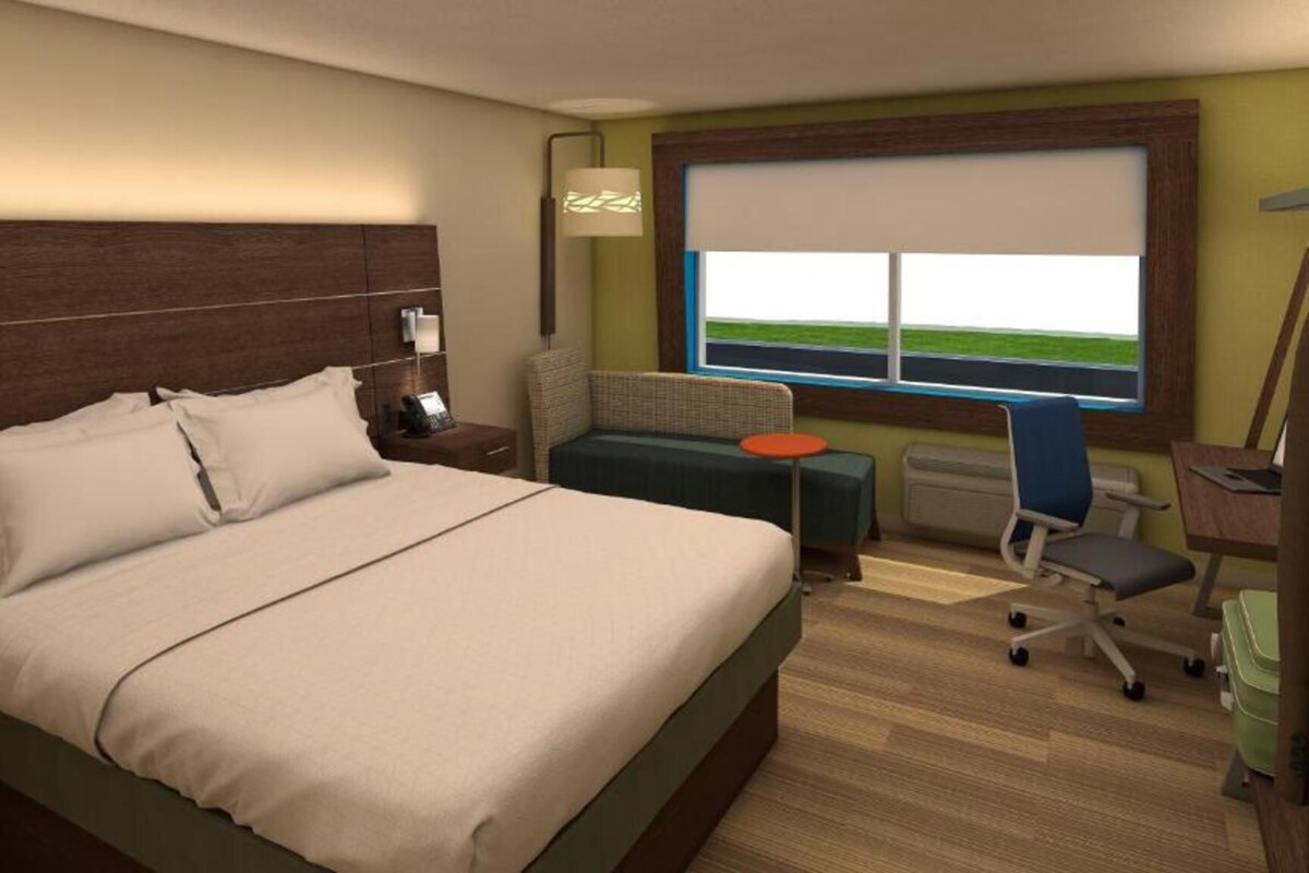 A hotel room with a large bed, a small sofa, a desk with a chair, a window with a view, and a lamp.