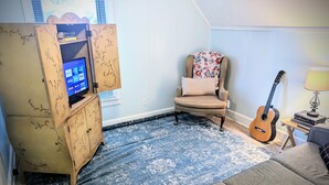 Una sala de estar con televisión, un sillón floral, una guitarra y un sofá.