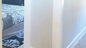 Un pasillo con piso de madera que conduce a un dormitorio con cama y ventilador de techo.