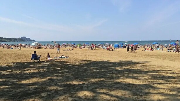 Una playa concurrida, gente y sombrillas.