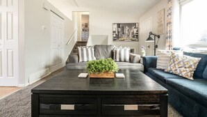 A living room with a dark coffee table, a blue sofa, and a staircase leading to another room. - "Central Springs" Super Cozy 4Bed / 2Bath Home GREAT Location! Click to see more (Colorado Springs)