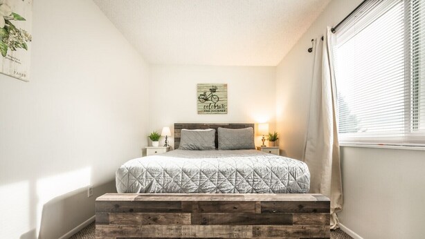 A bedroom with a bed, a headboard, bedside tables, a wall-mounted sign, and a window with blinds. - "Central Springs" Super Cozy 4Bed / 2Bath Home GREAT Location! Click to see more (Colorado Springs)