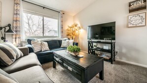 A living room with a sofa, coffee table, TV, and decorative items. - "Central Springs" Super Cozy 4Bed / 2Bath Home GREAT Location! Click to see more (Colorado Springs)