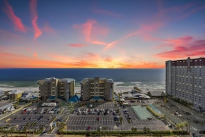 Un hôtel situé sur la côte, composé de plusieurs bâtiments, doté d’un parking et offrant une vue sur l’océan au coucher du soleil.