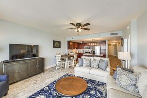 A living room with a TV, sofa, coffee table, and dining area with chairs.
