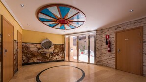 A lobby with a circular floor design, a large ceiling artwork, and a fire extinguisher on the wall.