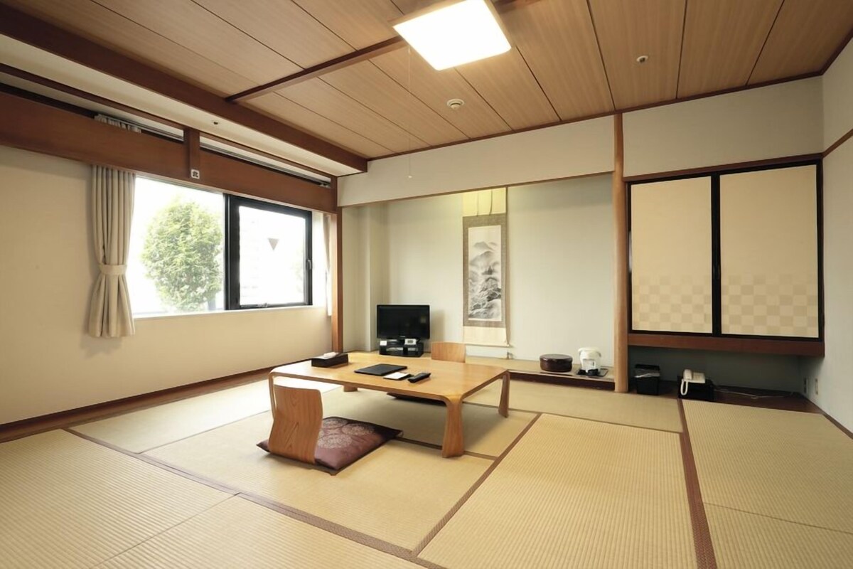 A traditional Japanese-style room with tatami flooring, a low wooden table, a television, and sliding doors.