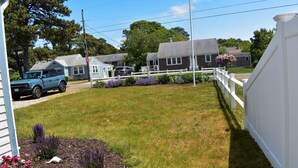 Un barrio residencial con una cerca blanca, césped y casas al fondo.