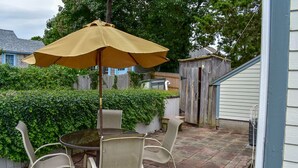 Un patio con mesa y sillas, un paraguas amarillo y un cobertizo de madera al fondo.