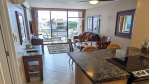 Una cocina amplia con una isla grande, un comedor con sofá y sillas, y vistas al exterior a través de ventanas amplias.