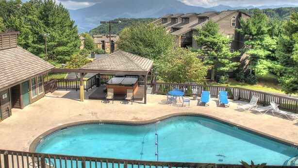 A pool area with a wooden deck, lounge chairs, and a gazebo.