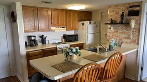 A compact kitchen with wooden cabinets, a stove, microwave, refrigerator, and a small island with chairs.