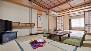 Una habitación japonesa tradicional con suelo de tatami, televisión, una mesa con juego de té y puertas correderas.