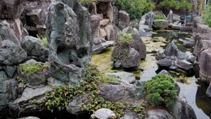Un jardín rocoso con un estanque, rodeado de grandes rocas y follaje.