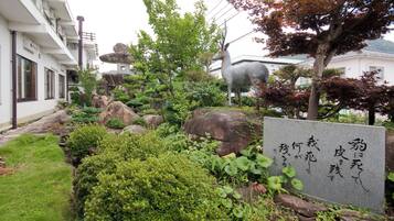 Un jardín ajardinado con una estatua de ciervo, rocas y una lápida de piedra con caracteres japoneses.
