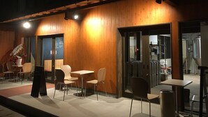 Un área de estar interior con paredes de madera y mesas, un menú en una pizarra y una escalera que sube a un nivel superior.