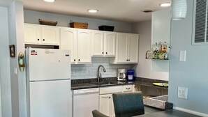 A modern kitchen with white cabinets, a built-in dishwasher, and a dining area with blue chairs.