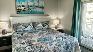 A bedroom with a bed, two bedside tables with lamps, a painting above the bed, and a view through a window.