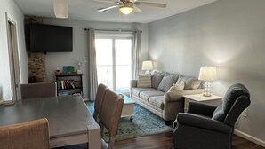 A modern living room with a dining table, chairs, a sofa, and a TV mounted on the wall.