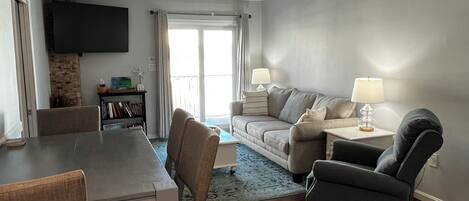 Una sala de estar moderna con una mesa de comedor, sillas, un sofá y un televisor montado en la pared.