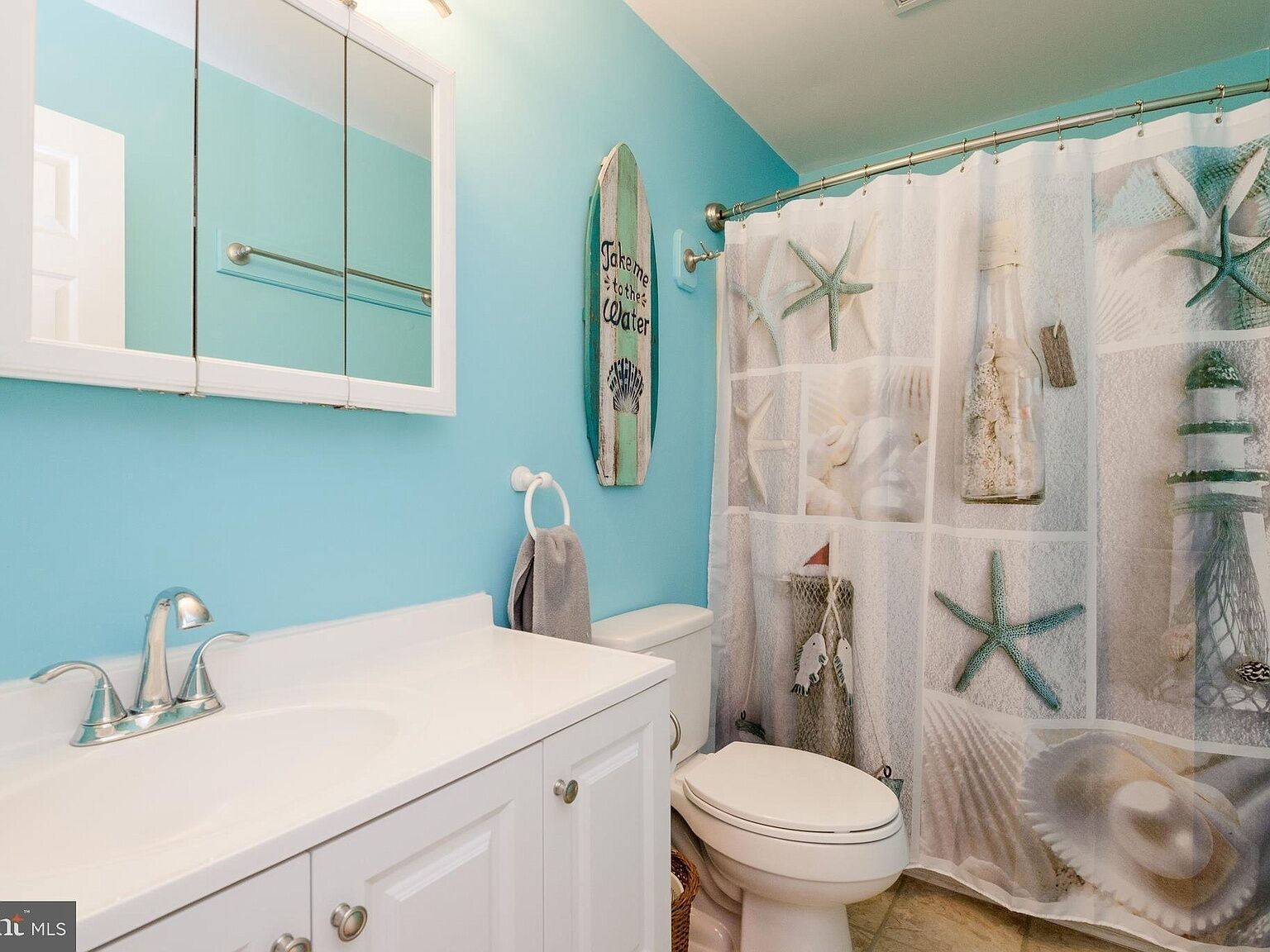 Een badkamer met een blauwe wand, een witte wastafel, een toilet en een douchegordijn met zeedecoratie.