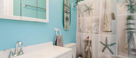 Een badkamer met een blauwe wand, een witte wastafel, een toilet en een douchegordijn met zeedecoratie.