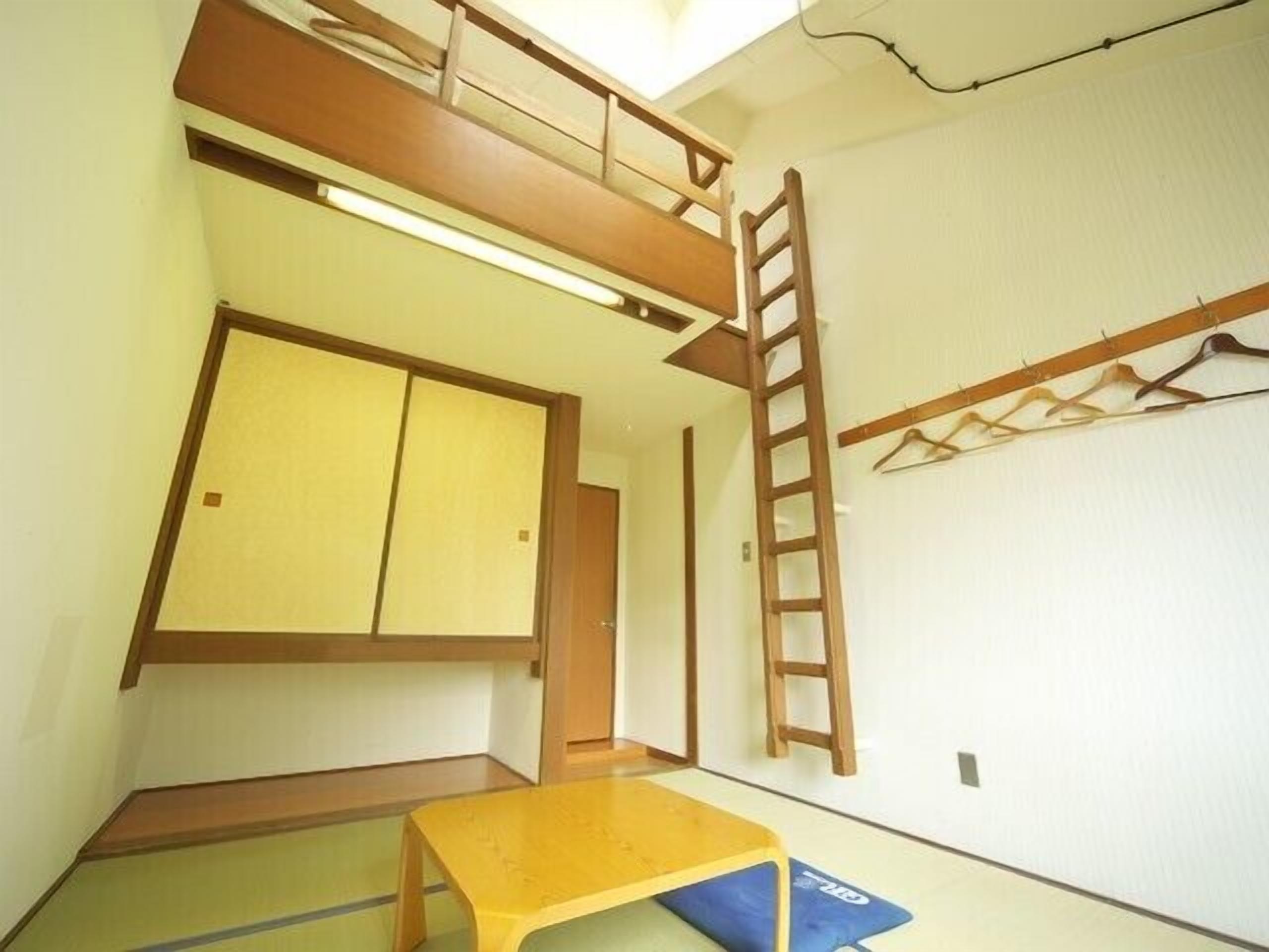 A room with a bunk bed, a ladder, a table, and a futon.