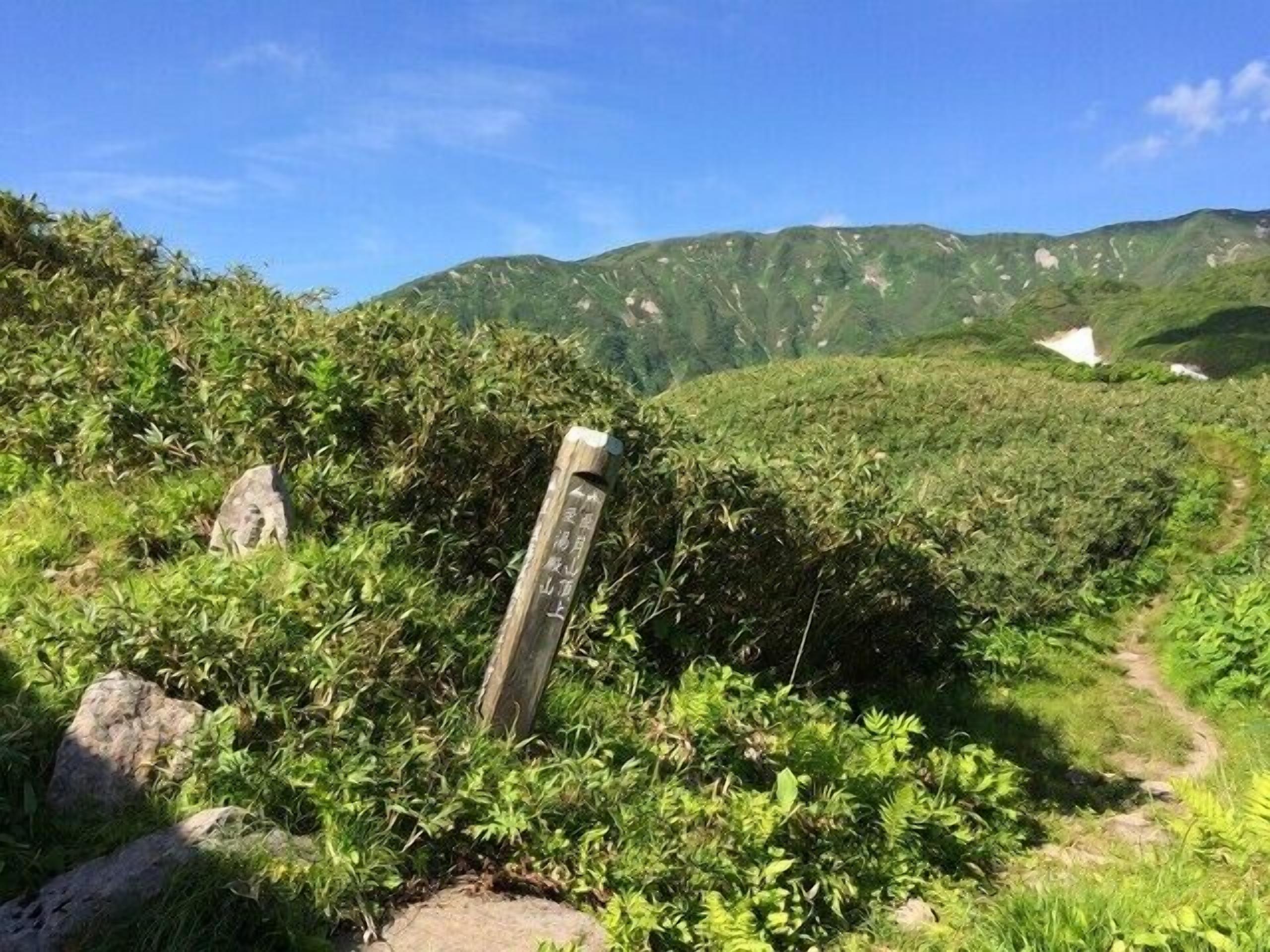 A natural landscape with a stone marker, a path, and green hills in the background.