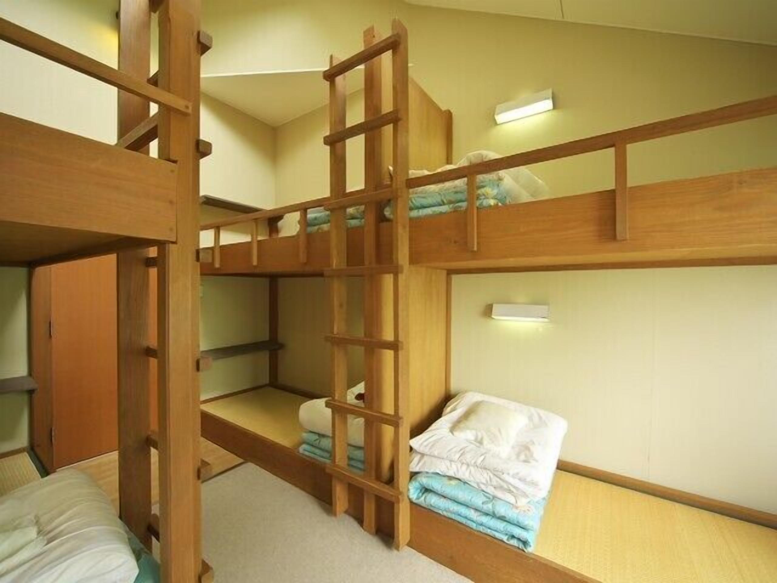 A bunk bed room with a ladder, a small shelf, and a wall-mounted light.