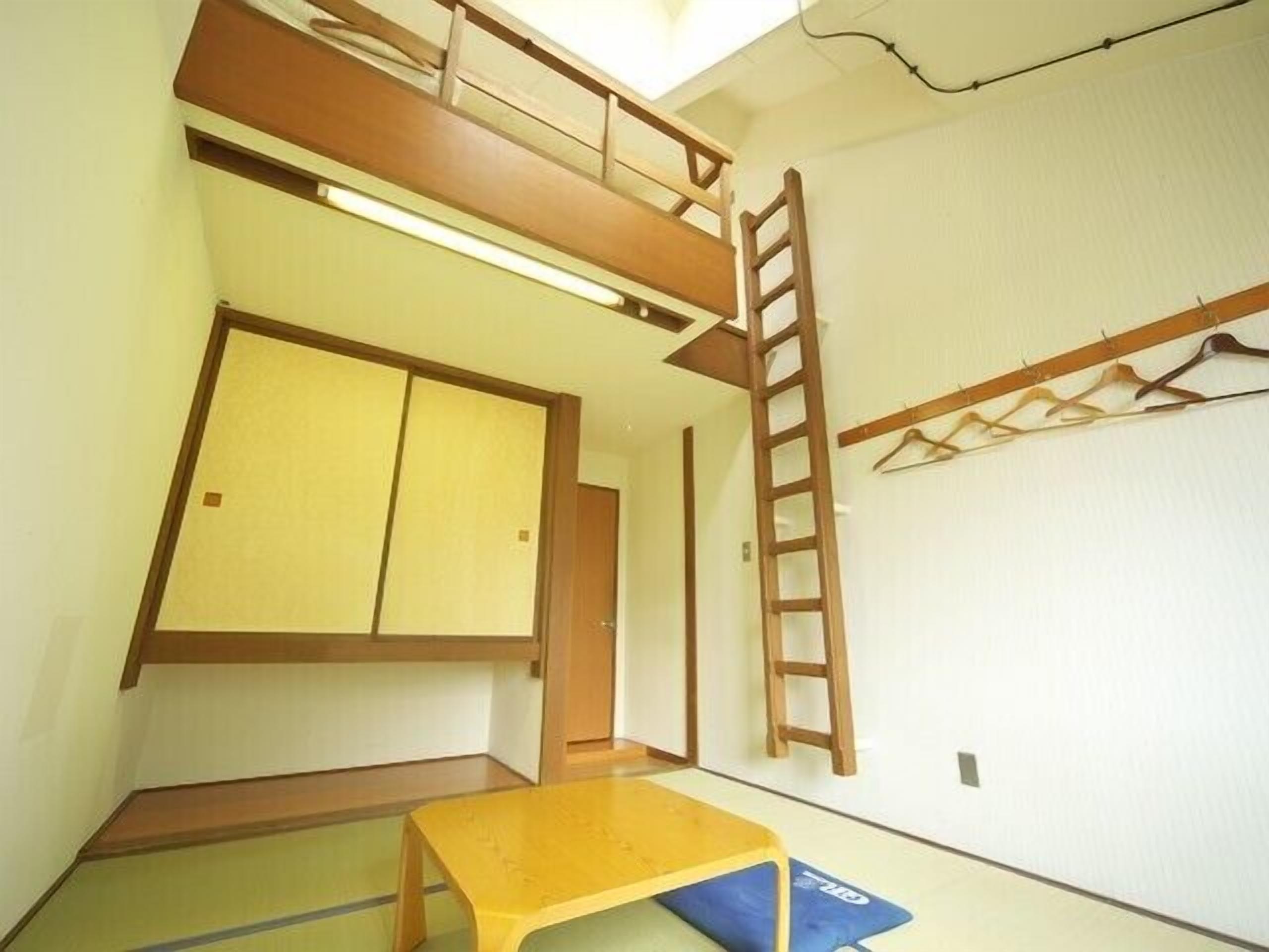 A room with a bunk bed, a ladder, a table, and a futon.