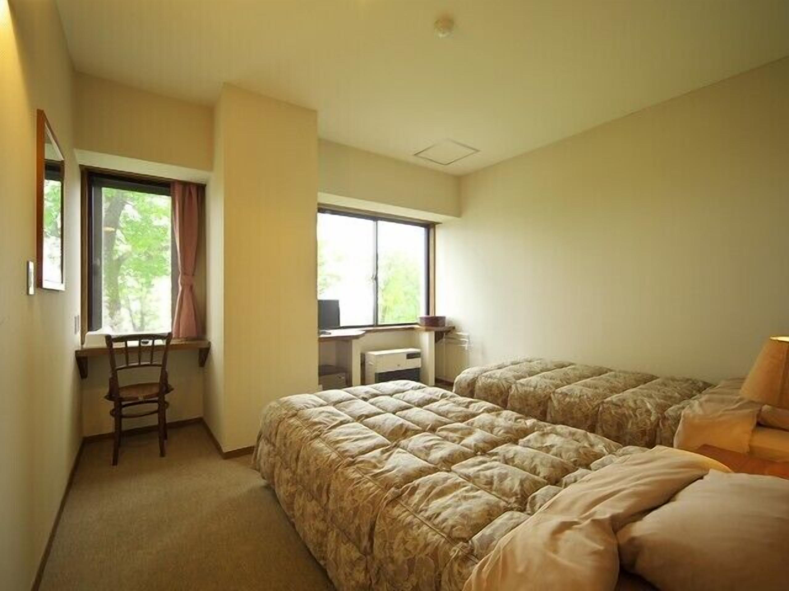 A bedroom with two beds, a desk, a chair, and a window.