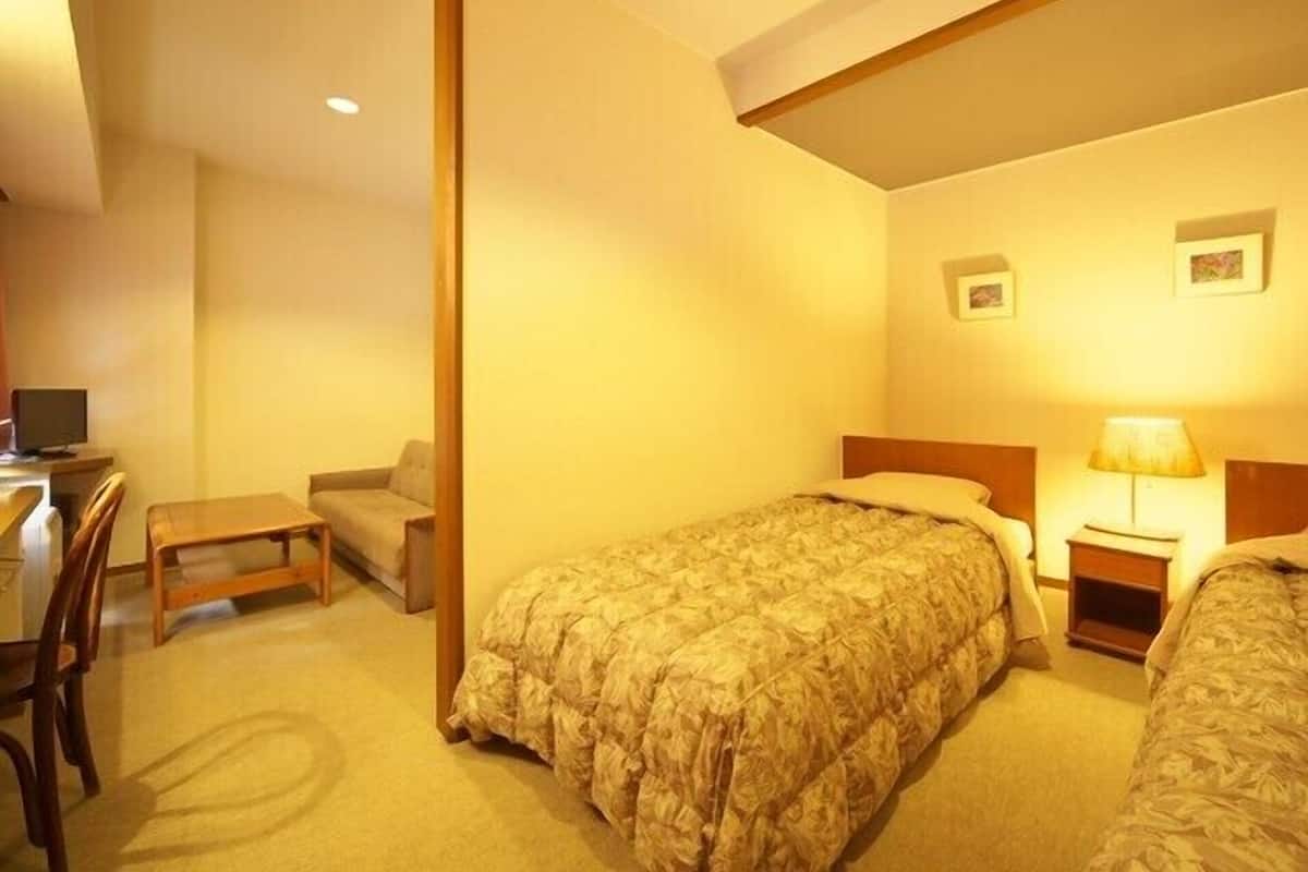 Una habitación de hotel con una cama individual, un escritorio con una silla y una mesita.