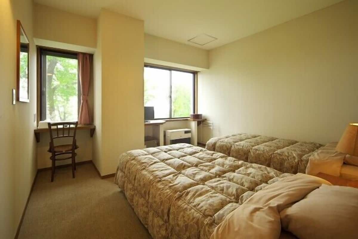 Un dormitorio con dos camas, un escritorio, una silla y una ventana.