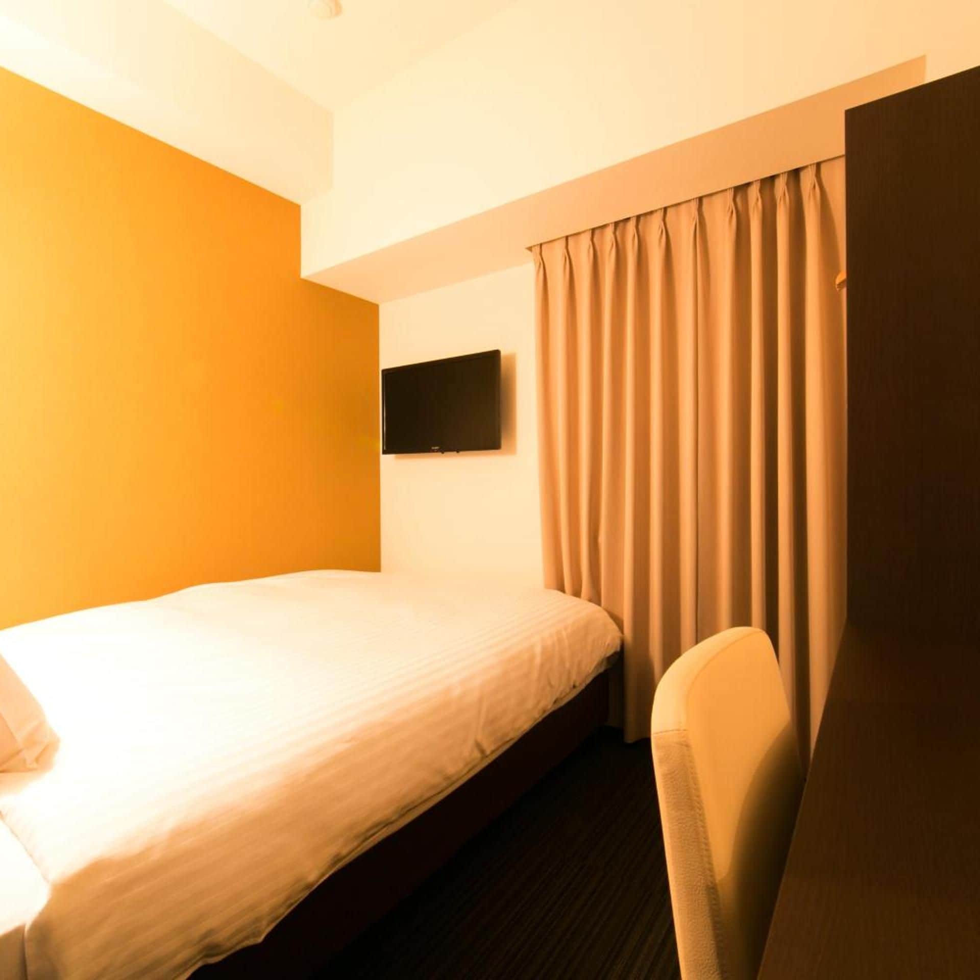 Habitación de hotel con una cama individual, un televisor de pantalla plana montado en la pared y una silla.