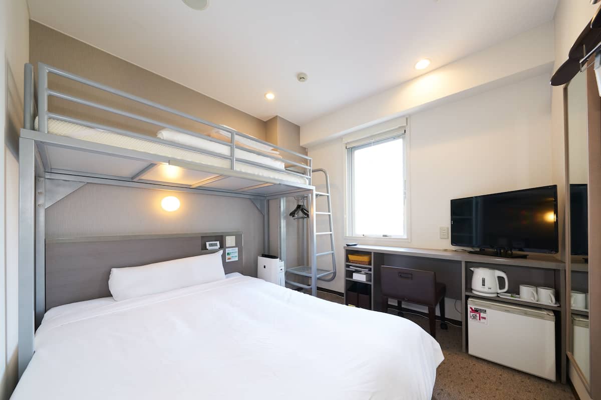 Een hotelkamer met een stapelbed, bureau, televisie en kitchenette.