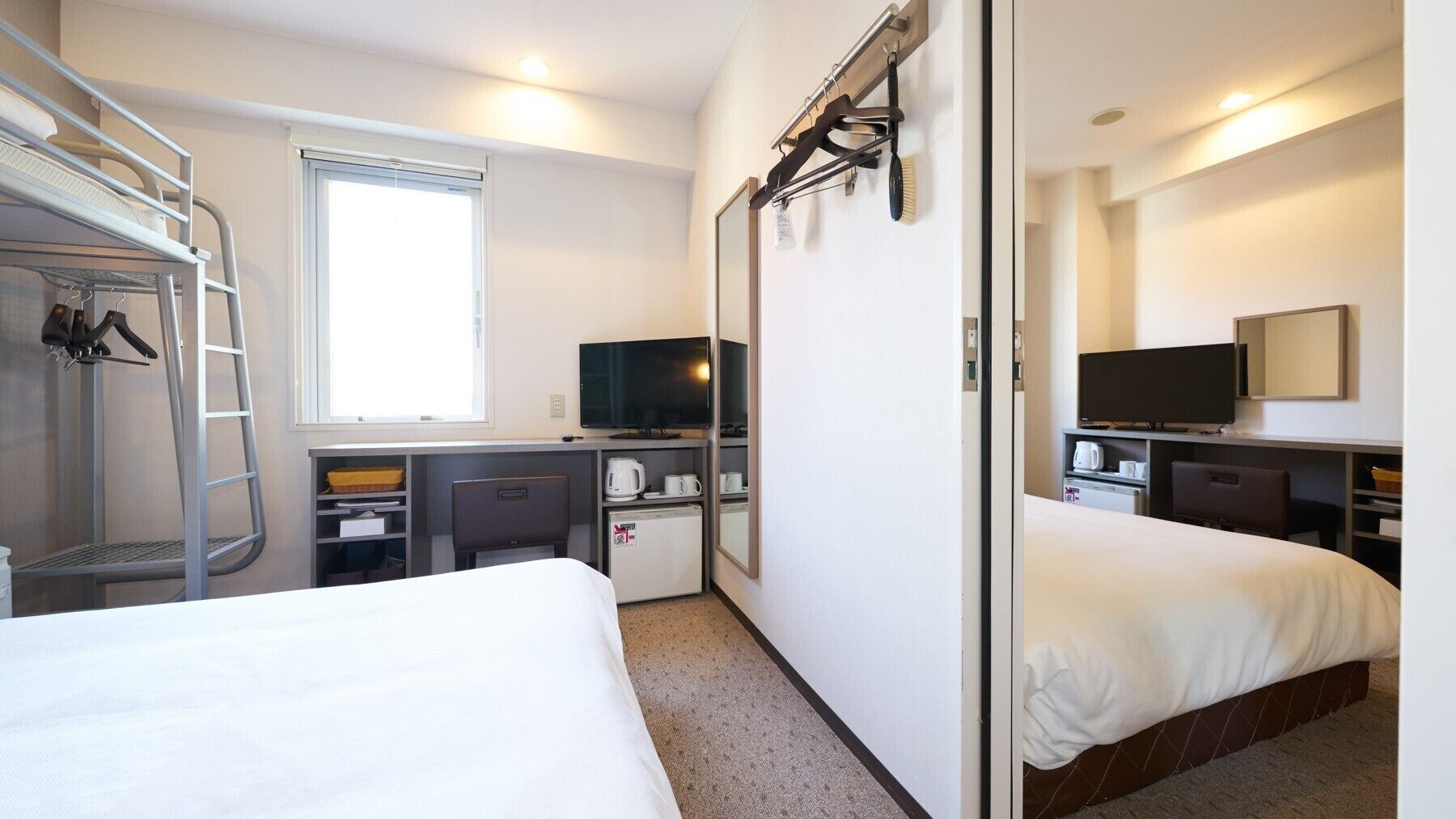Een hotelkamer met een stapelbed, een bureau met een computer, een televisie, een kleine koelkast en een spiegel.