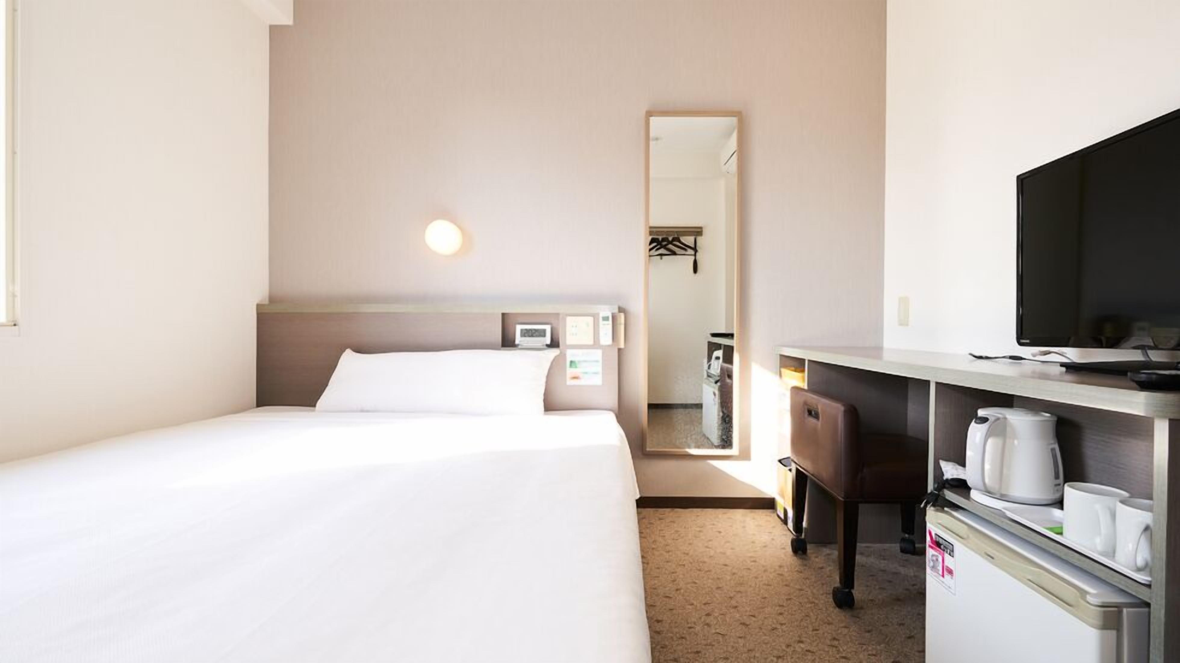 Een hotelkamer met twee bedden, een bureau met een televisie, een koffiezetapparaat en een spiegel.
