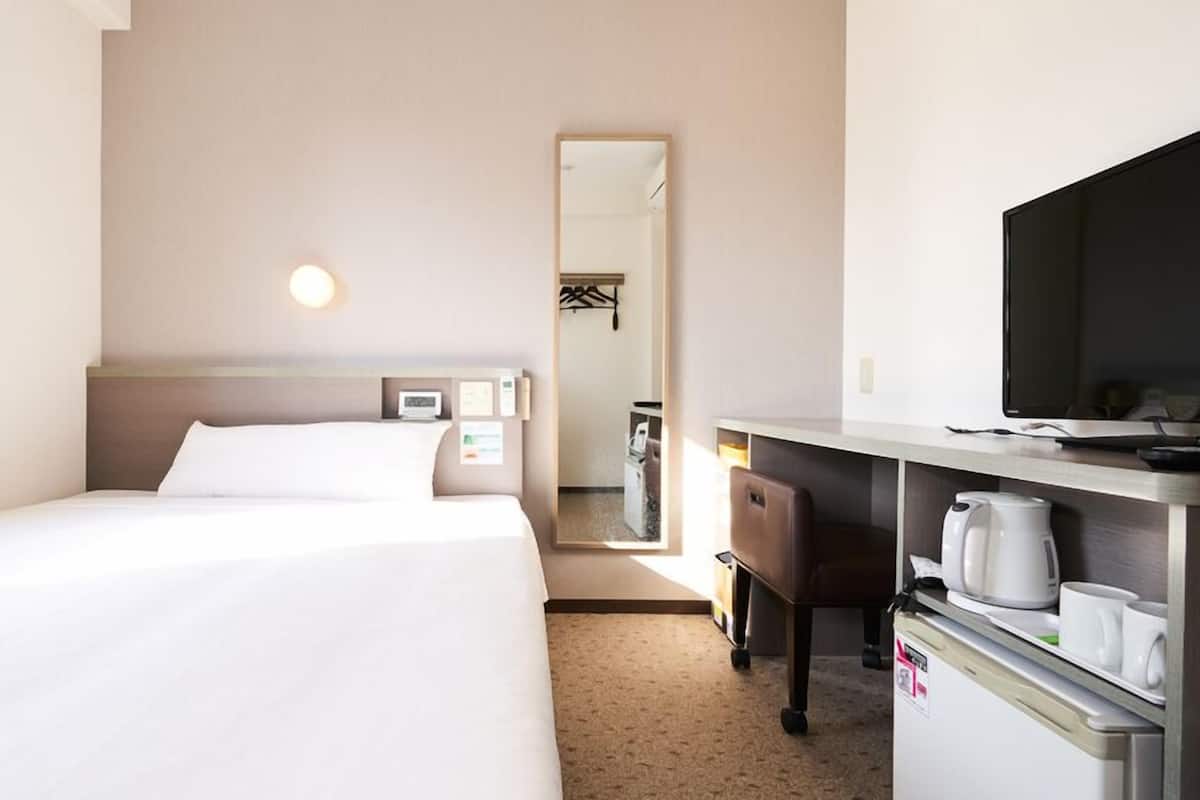 Een hotelkamer met twee bedden, een bureau met een televisie, een koffiezetapparaat en een spiegel.