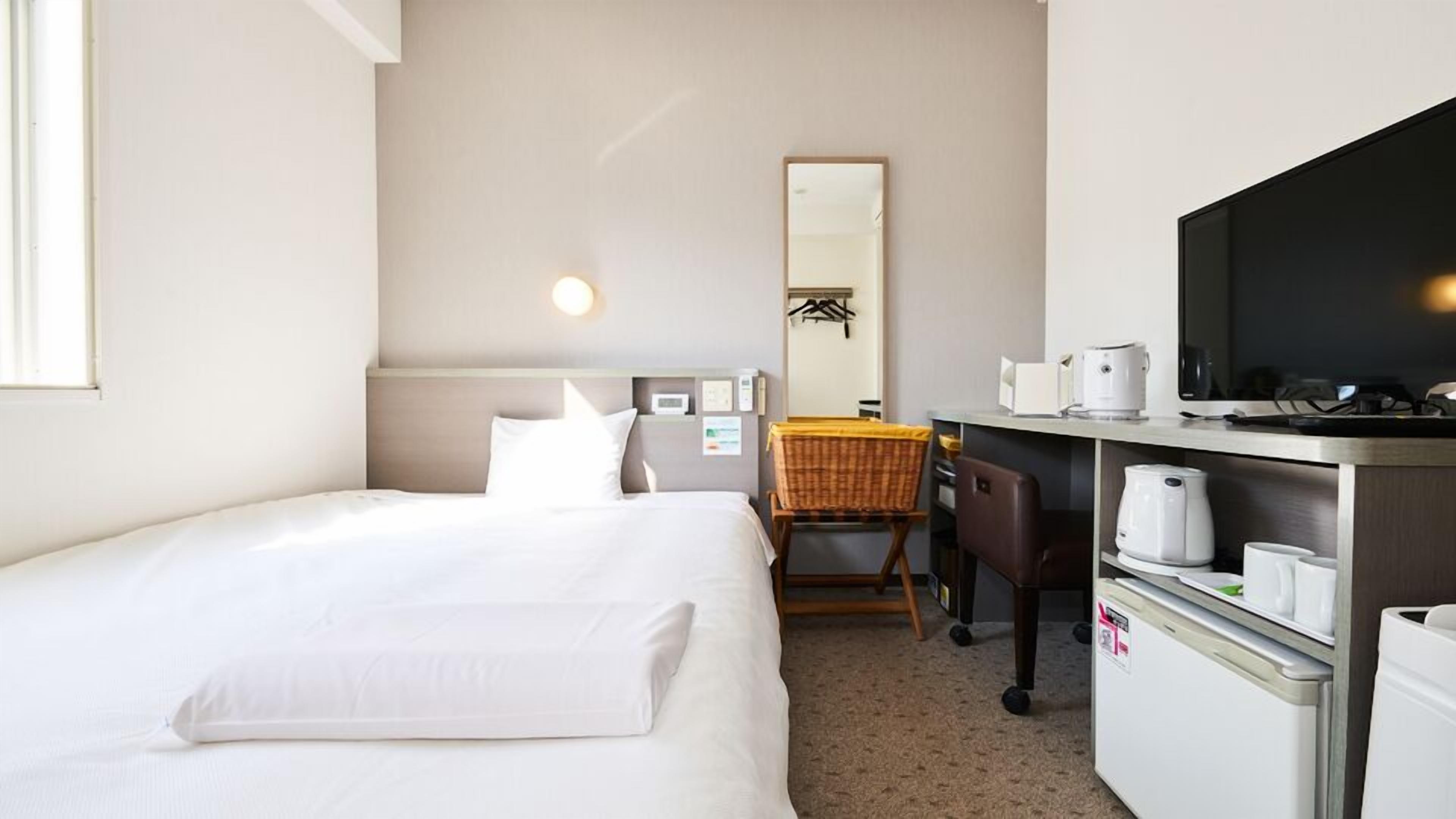 Een hotelkamer met een bed, een bureau met een stoel, een magnetron, een koffiezetapparaat en een televisie.
