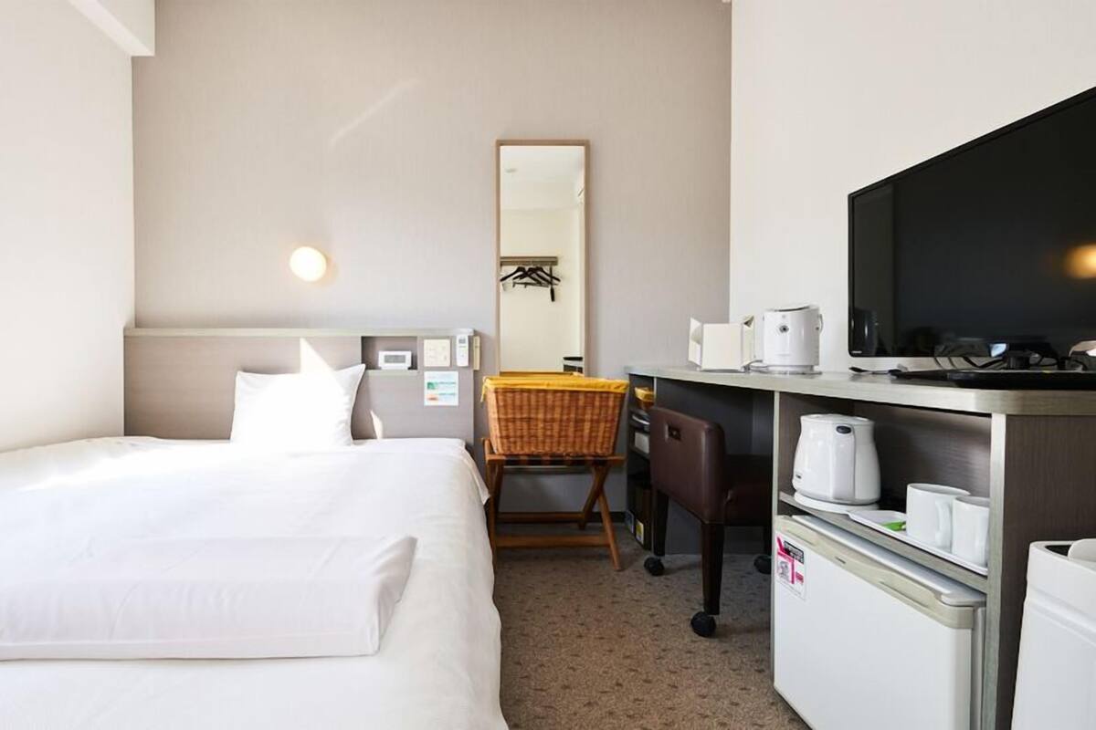 Een hotelkamer met een bed, een bureau met een stoel, een magnetron, een koffiezetapparaat en een televisie.