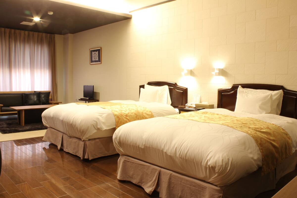 A hotel room with two beds, a desk, a chair, and a television.