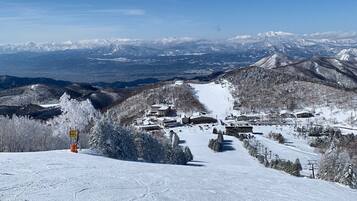 A snow-covered mountain resort with multiple buildings, ski slopes, and a clear view of distant snow-capped peaks.