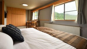 Een slaapkamer met een bed, een bureau en een raam met uitzicht op groene heuvels.